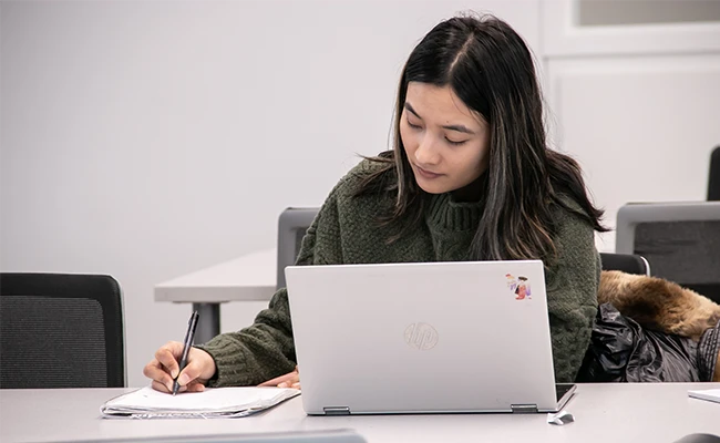 a young woman looks at a laptop while writing