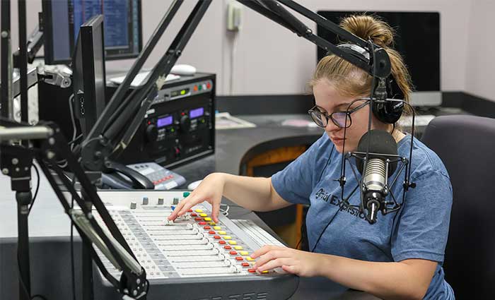 a students sits in a booth djing a radio station