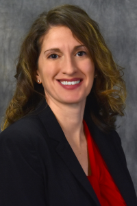Headshot of woman with curly brown hair in a red blouse and black blazer.