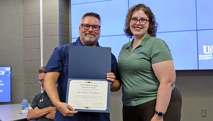Dr. Christopher Strickland receiving the certificate for Outstanding Innovation in 在线 Teaching award from the previous year's winner, Dr. Amanda Sladek.