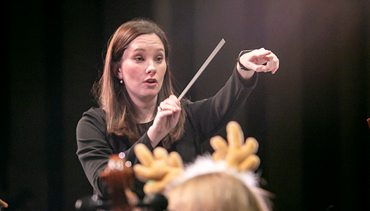 A woman conductor leads an orchestra concert. 