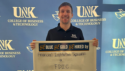 Logan Shaw holding a sign that reads, "Be Blue. Be Gold. Be Hired by Financial Institution Specialist at FDIC."