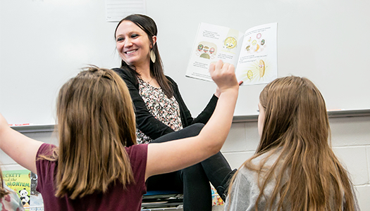 Woman reading a book to young children in a classroom.