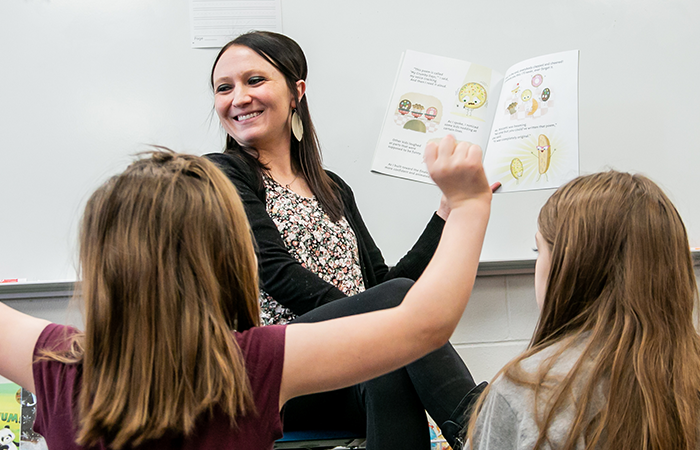 A teacher engaging with young students while reading an illustrated book during a classroom session.