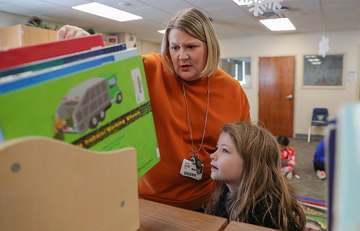 A teacher and a young student exploring colorful books together in a classroom, fostering a love for reading.