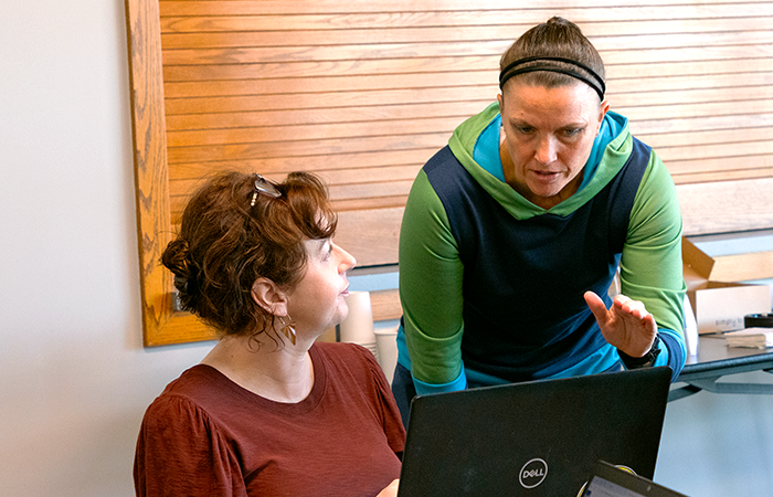 Two women engaged in a collaborative discussion over a laptop in a modern workspace.