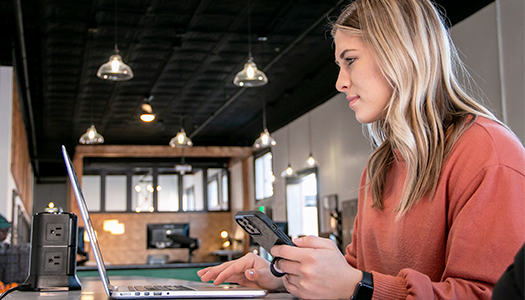 a woman holding a cup of coffee sits at a table with a laptop