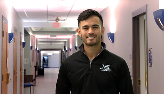 arron stands in a hallway wearing a black quarter-zip pullover embroidered with “太阳城娱乐官网 Master of Business 政府.”