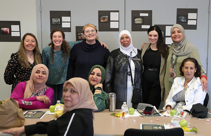 A group of women smiling together in a community setting, some are sitting and others are standing with their arms around each other.