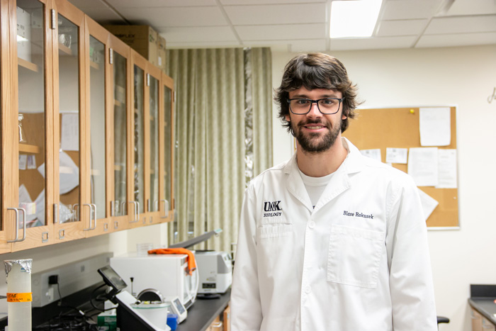 Blase Rokusek smiles while wearing a white lab coat in a 太阳城娱乐官网 biology lab.