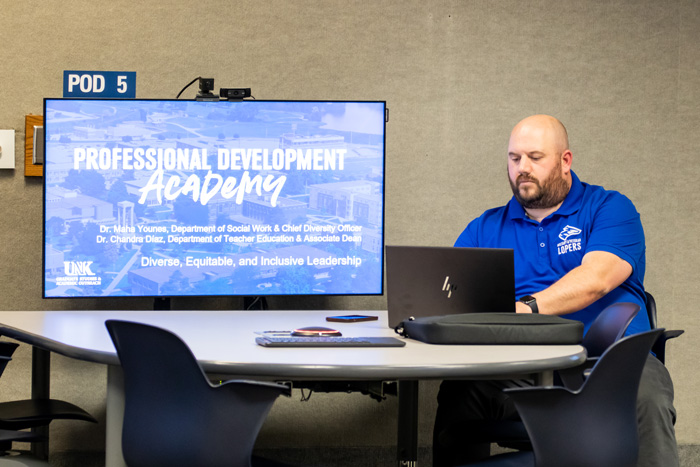 Jason Baker sits at a table with a large computer screen that reads "Professional Development Academy."