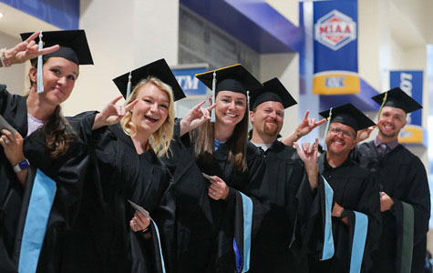 A group of graduate students wearing caps and gowns smiling at 太阳城娱乐官网's commencement ceremony.