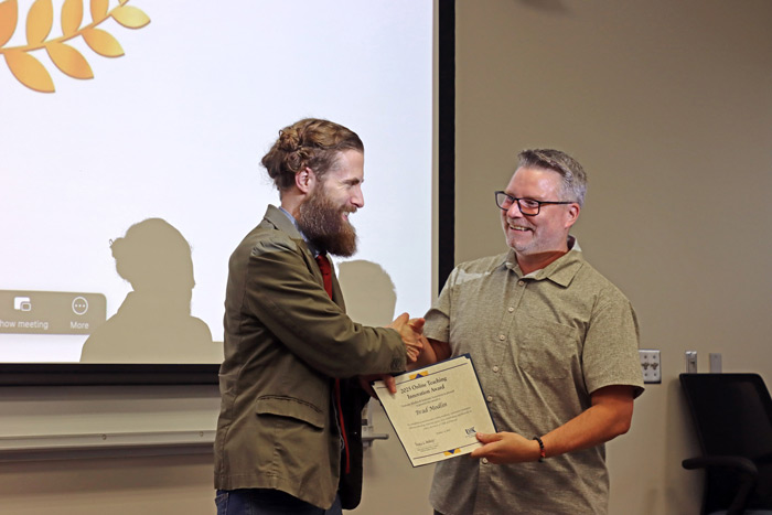 Two men shaking hands during a certificate presentation ceremony. One man is presenting a certificate to the other, who is smiling.