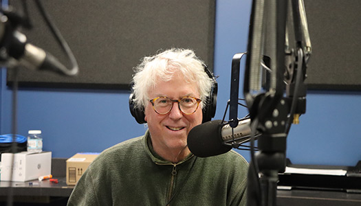 Rick Brown smiling behind a microphone in a radio studio.