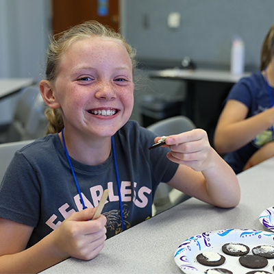 a young girl smiles at the camera while working on a craft project
