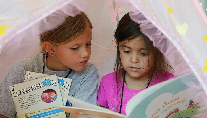 two students read books together in a tent