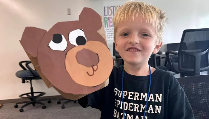 a student holds up a homemade paper bag bear puppet