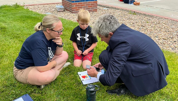 a student sits in the grass while two instructors show him an activity