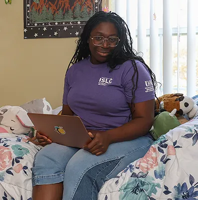 a student sits on her bed with a laptop