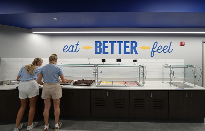 students serve themselves food in front of a sign that says eat better, feel better