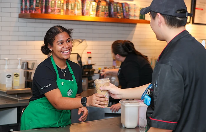a worker passes a starbucks coffee to a customer