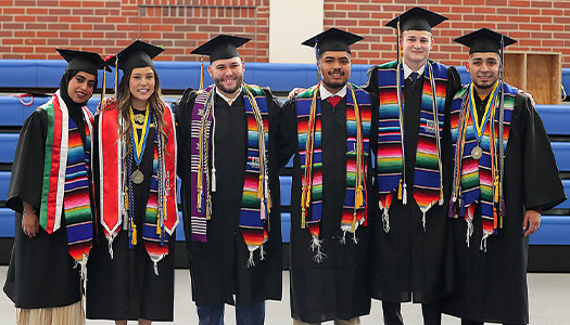 students pose for a photo at commencement in their caps, gowns, and stoles